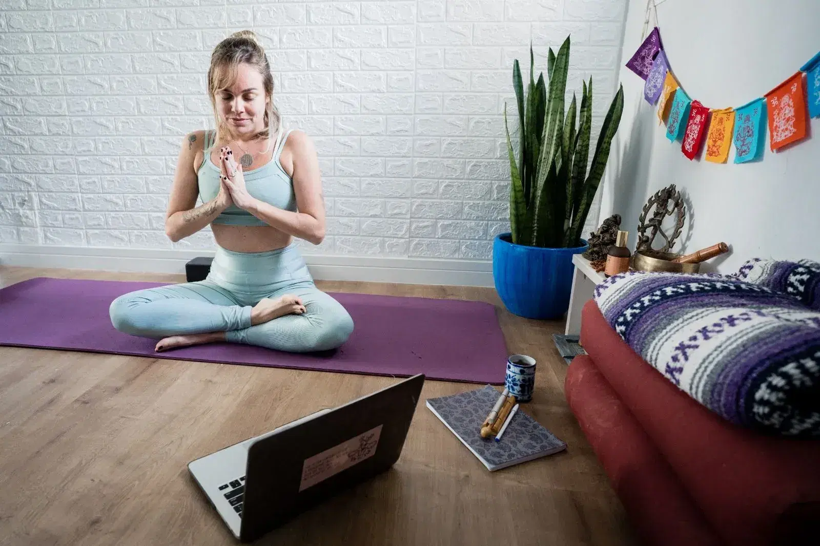 Mulher sentada sobre tapate de yoga roxo em sala de meditação.